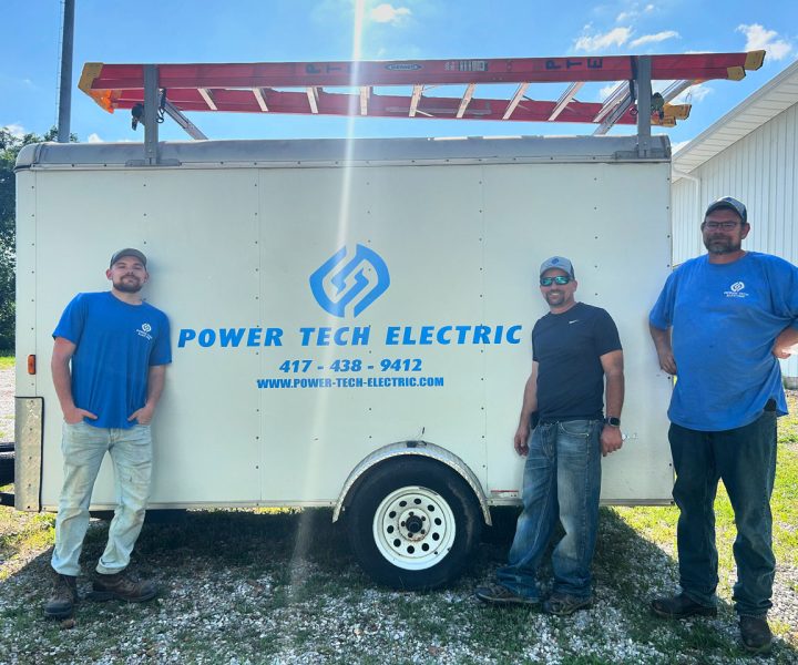 Three electricians standing in front of a branded work trailer, representing the skilled team behind reliable electrical services.