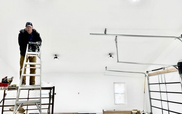 An electrician installs recessed lighting in a garage, showcasing residential electrical renovation services.