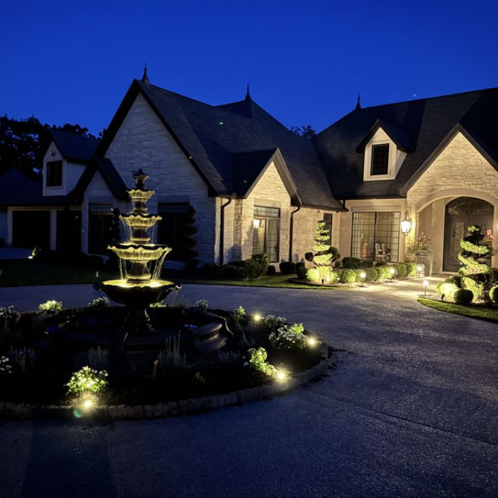 A beautifully lit home exterior with warm lighting around the entrance and landscaping, demonstrating expert residential lighting design.