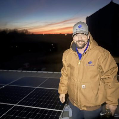 An electrician standing on a roof with installed solar panels, highlighting expertise in solar energy solutions.
